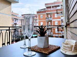 A balcony with two clear glasses, a small potted plant, and a miniature Colosseum model on a coaster.