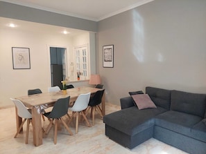 Una sala de estar moderna con un sofá gris, una mesa de comedor con sillas y obras de arte enmarcadas en las paredes.