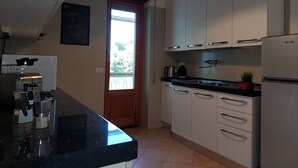Una cocina con armarios blancos, encimera negra, cafetera y ventana con vistas.