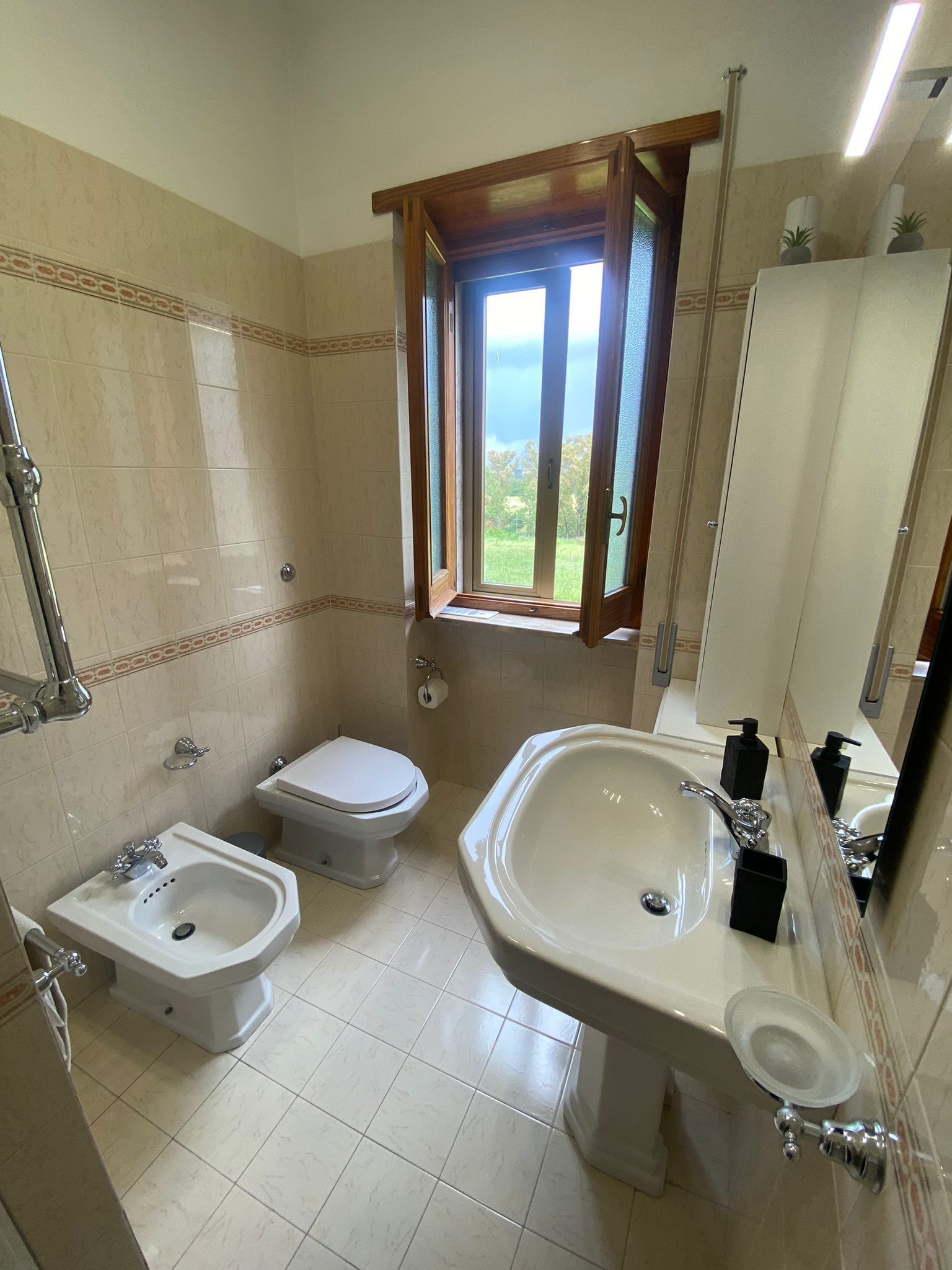 A bathroom with a toilet, bidet, sink, and a large mirror.