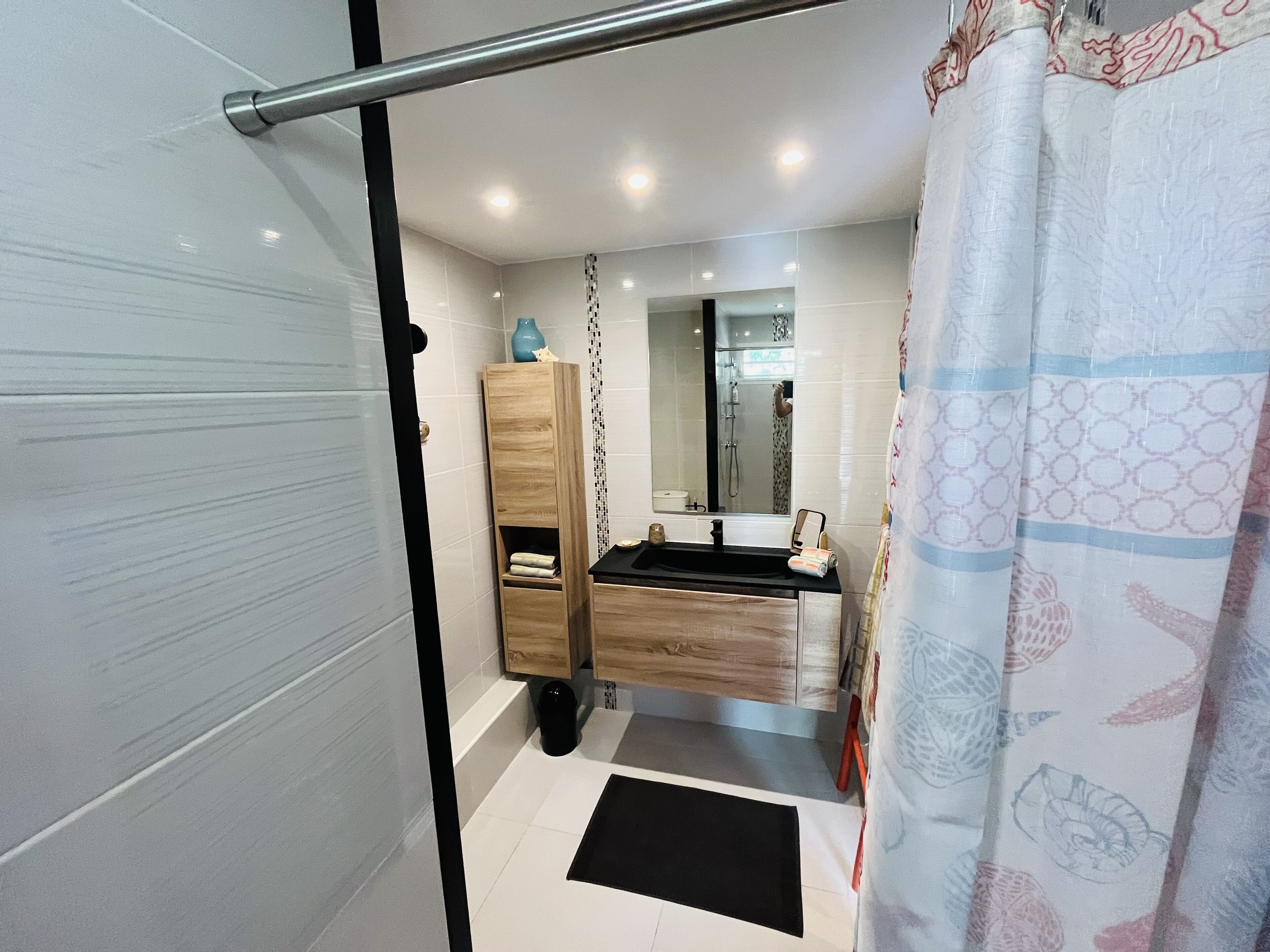 A modern bathroom with a glass shower enclosure, a wooden vanity, a black sink, and a patterned shower curtain.