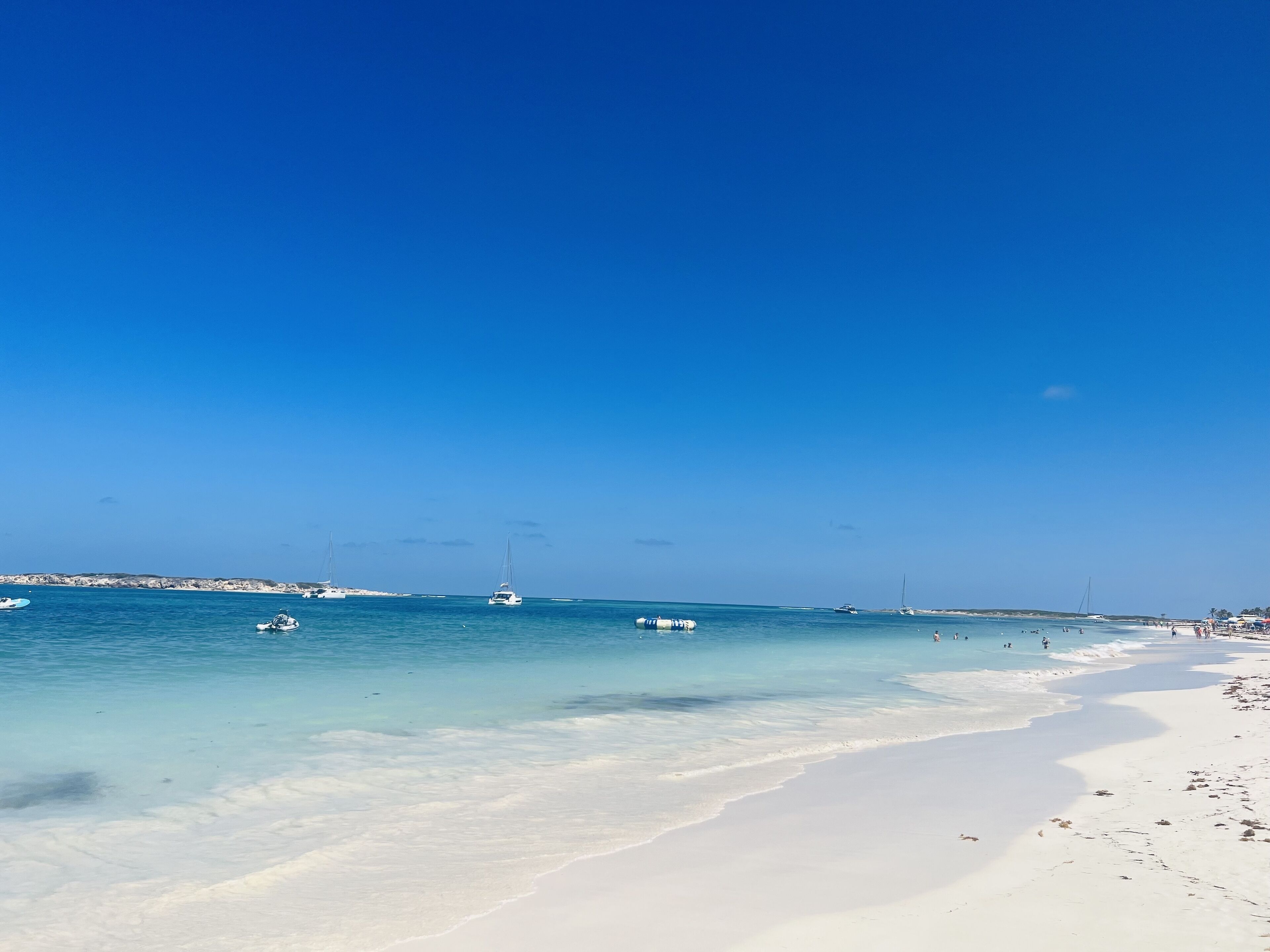 A beach with clear blue water, white sand, and boats.