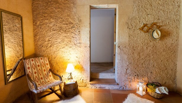 A rustic room with a stone wall, a wooden chair, a lamp, a lantern, and a basket with items. - Authentic apartment (Sineu)