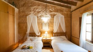 A room with two beds, each with white bedding and a canopy. There is a nightstand with a lamp between the beds. The walls are textured and the room has a rustic wooden ceiling. - Authentic apartment (Sineu)
