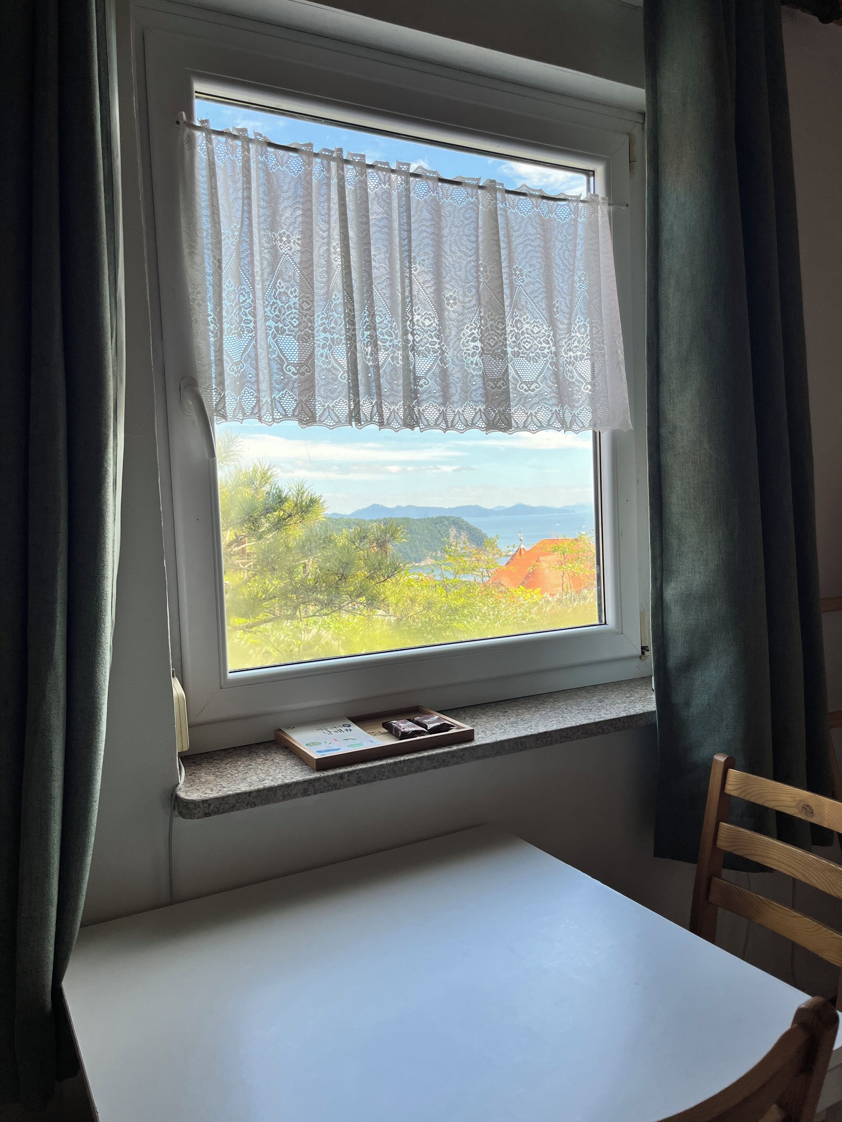 A room with a window overlooking a scenic landscape, a table, and a chair.