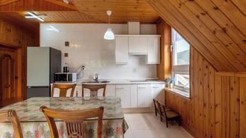 A wooden cabin kitchen with a dining table, chairs, a refrigerator, microwave, and cabinets.