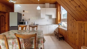 Een keuken met houten wanden, een eettafel met stoelen, een koelkast, een magnetron, en een raam met uitzicht.