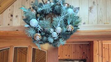 A wooden cabin interior with a Christmas wreath, a framed painting, and a seating area with a coffee machine.