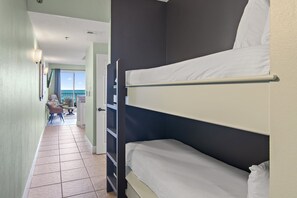 Une chambre avec des lits superposés donnant sur l’océan, un couloir avec des chaises et une porte menant à un balcon.