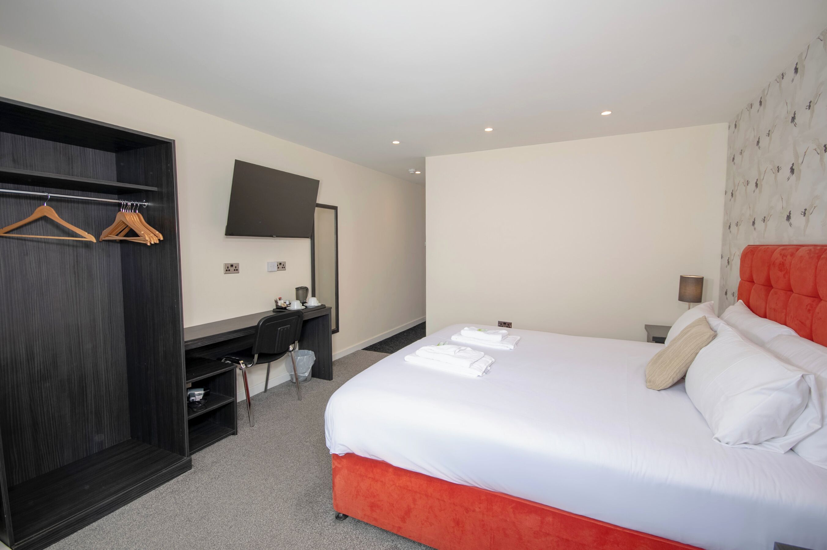 Une chambre d’hôtel avec un lit, un bureau, une armoire et un téléviseur fixé au mur.