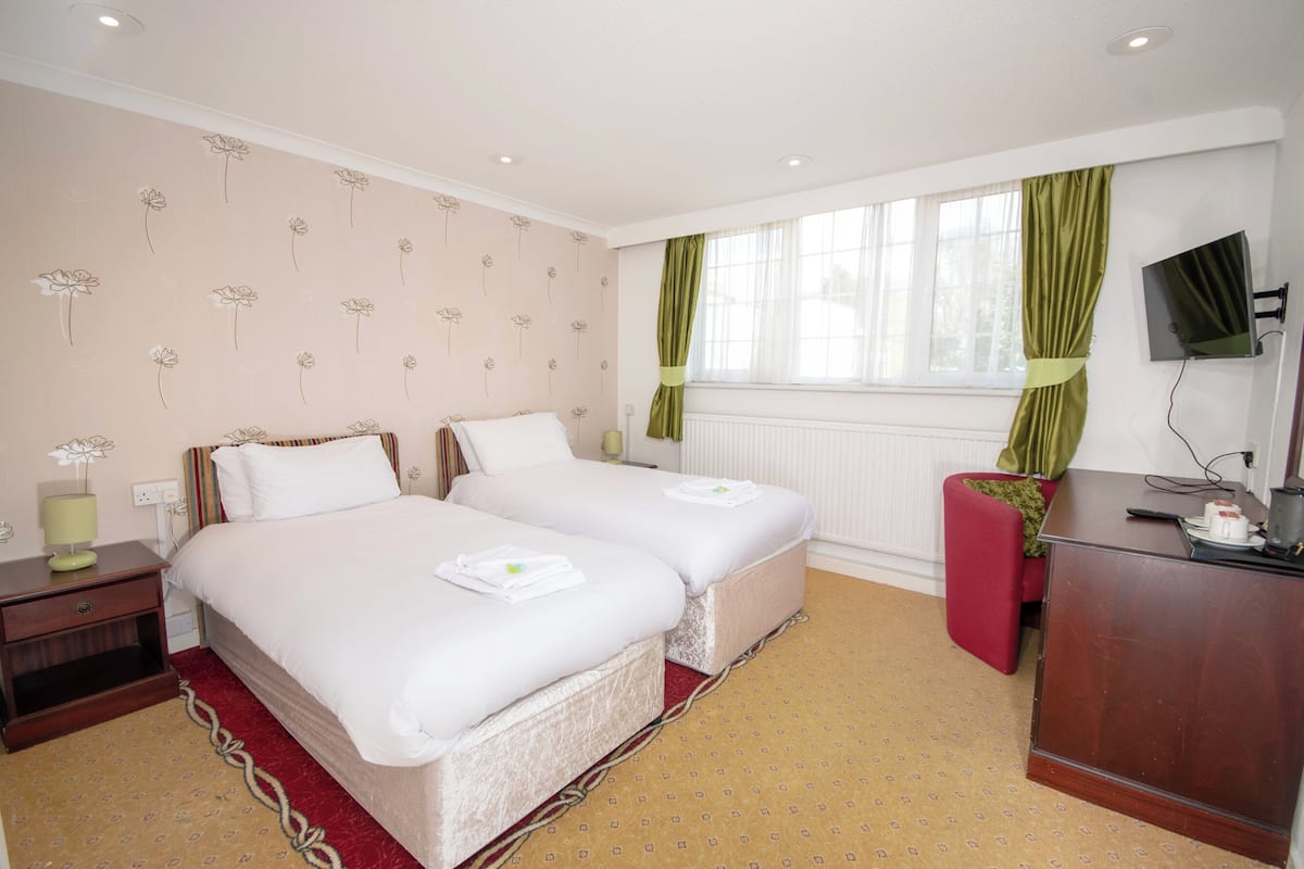 A hotel room with two beds, a desk, a TV, and a window with curtains.