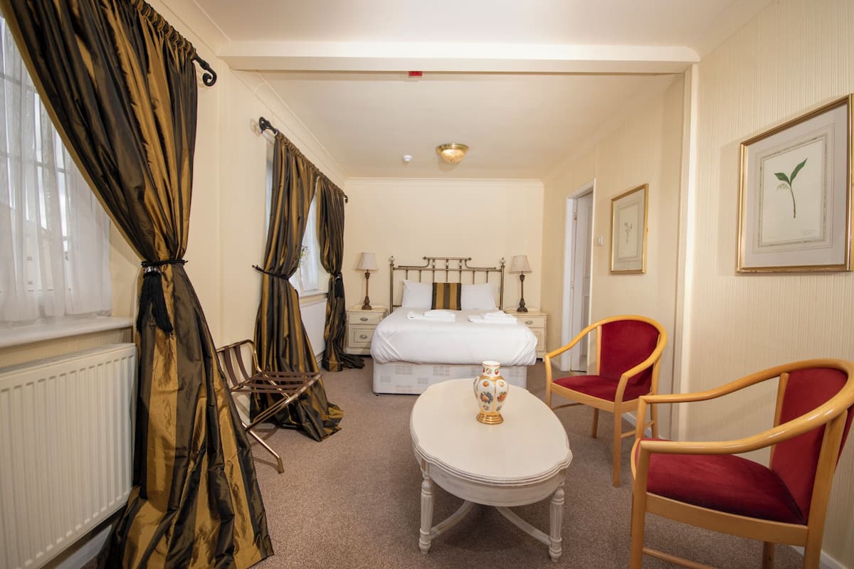 A hotel room with a bed, two chairs, a table, and a window with curtains.