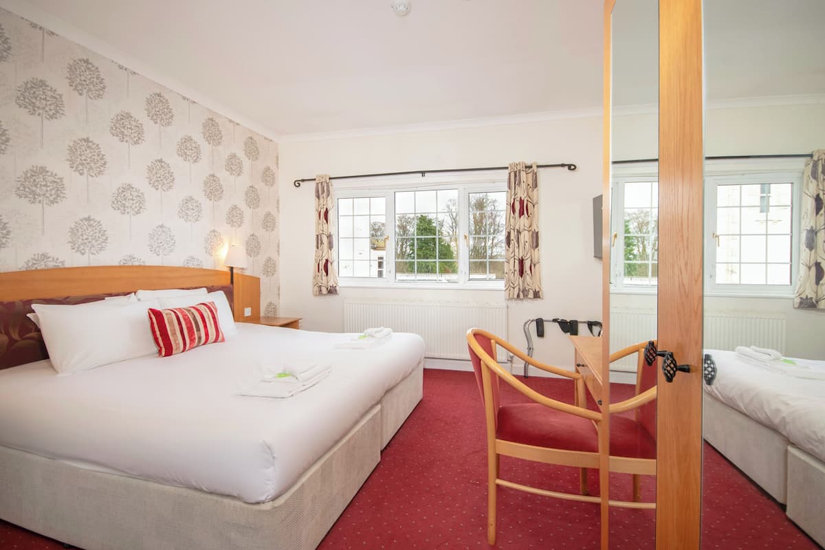 A hotel room with a large bed, a wooden chair, a window with curtains, and a radiator.