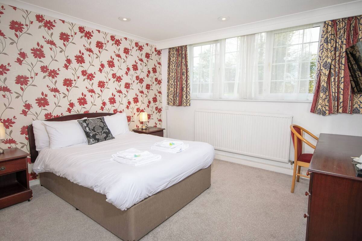 A neatly arranged hotel room with a large bed, a wooden nightstand, a desk, and a chair.