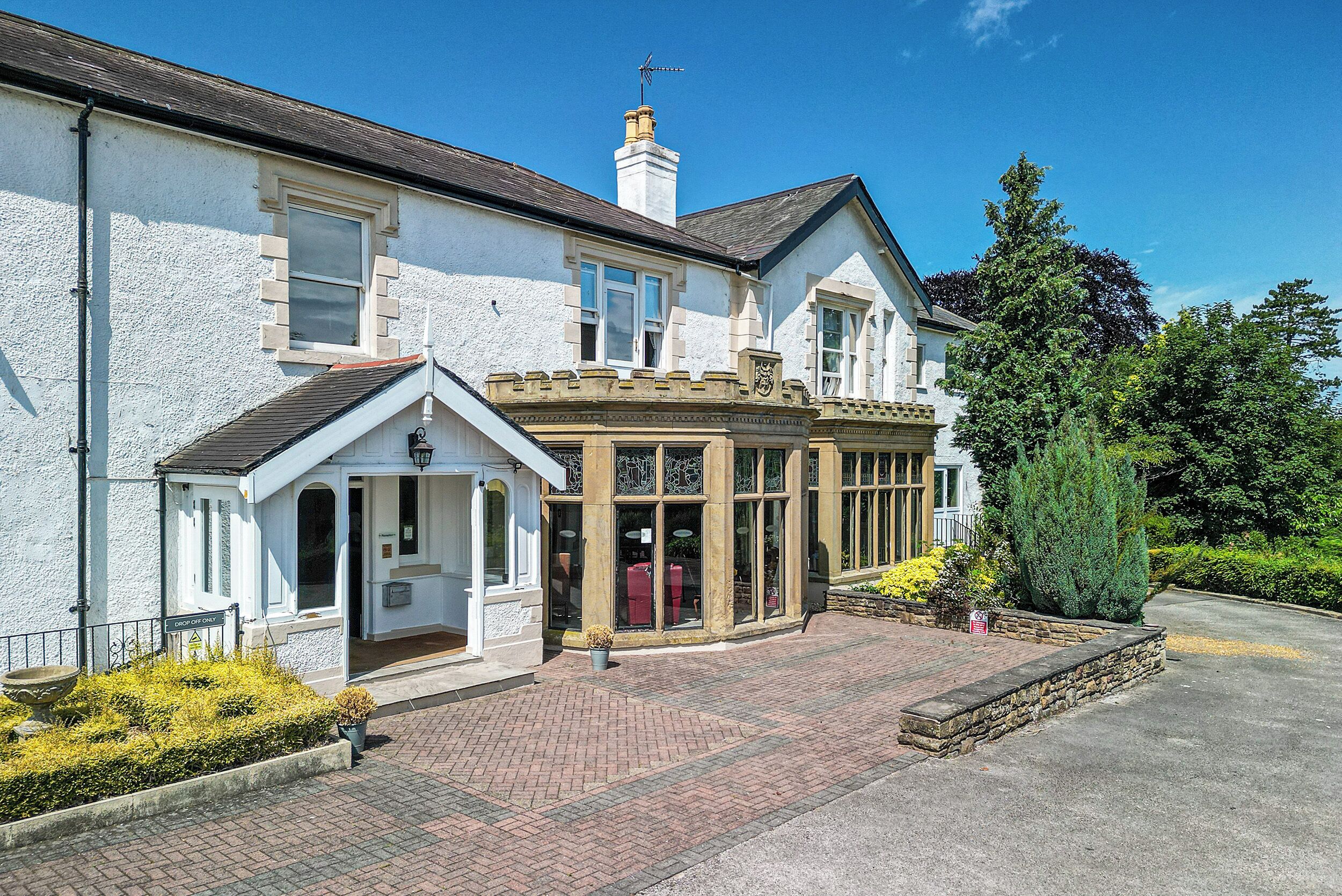 A traditional building with a white facade, a corner entrance, and a brick pathway leading to the entrance.