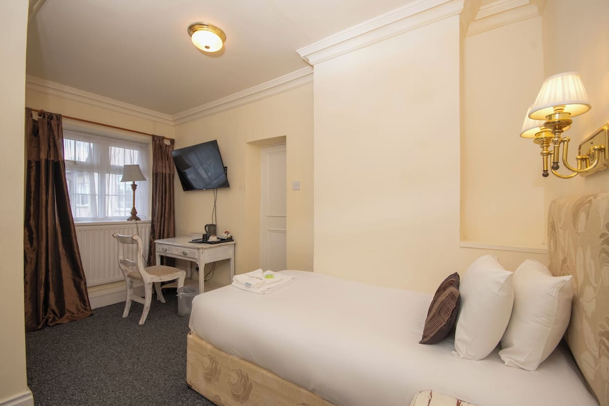 A hotel room with a bed, a desk, a chair, a television, and a wall-mounted lamp.