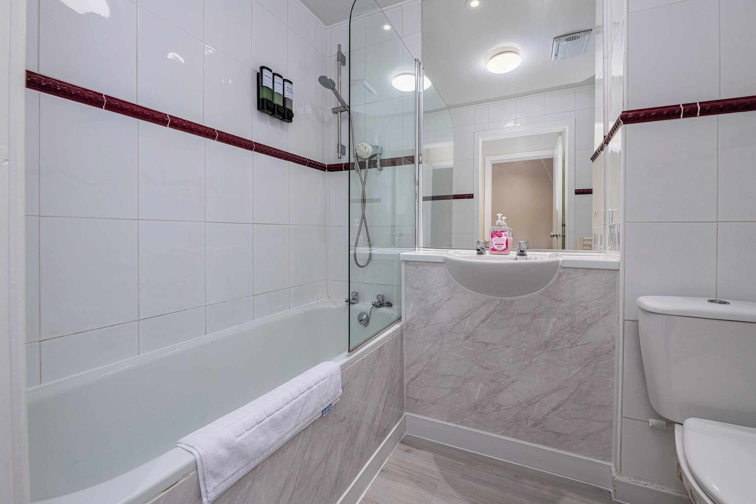 A modern bathroom with a glass-enclosed shower, a white bathtub, and a marble vanity.
