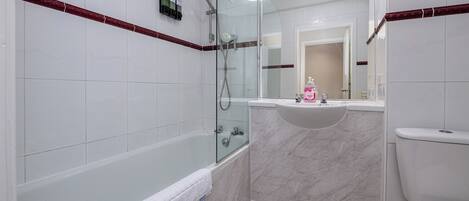 A modern bathroom with a glass-enclosed shower, a white bathtub, and a marble vanity.