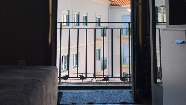 Et værelse med en seng, en dør til en balkon og udsigt til bygninger med røde tegltage.
