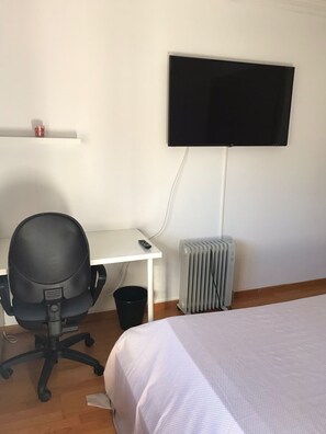 Une pièce comprenant un lit, un bureau avec une chaise, un téléviseur fixé au mur et un radiateur.
