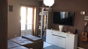 En stue med sofa, skærmpude, fjernsyn, guitar og et skab.