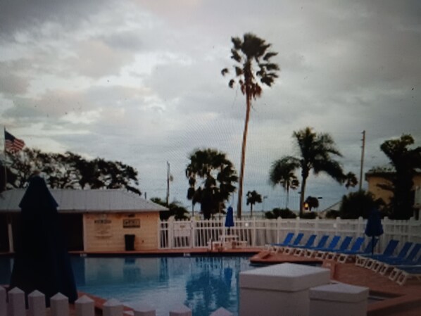 A swimming pool with a white fence, palm trees, and a building with an American flag.