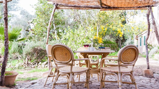 A rustic outdoor seating area with wicker chairs and a table, surrounded by greenery and a stone floor. - Family apartment Ca l'Amo (Sineu)