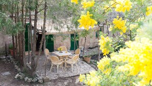 An outdoor patio with a table and chairs, surrounded by trees and yellow flowering plants. - Family apartment Ca l'Amo (Sineu)