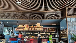 Ein Restaurant mit modernem Interieur, das eine Holzbalkendecke, eine Theke mit verschiedenen Gerichten und farbenfrohe Stühle zeigt.