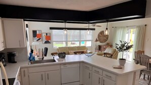 A modern kitchen with white cabinets, a central island, and a dining area with a chair and table. - New on Market ! Beautiful family home close to beach, golf, tennis and shopping. (Venice)