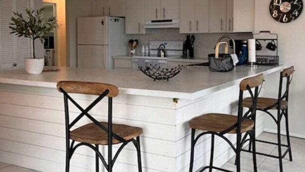 A modern kitchen with a central island, bar stools, pendant lighting, and a clock on the wall. - New on Market ! Beautiful family home close to beach, golf, tennis and shopping. (Venice)
