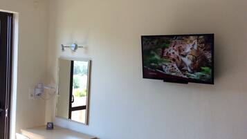 Un baño moderno con un tocador blanco, un espejo, un televisor montado en la pared y una ventana que proporciona luz natural.