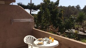 A balcony with a round table and two white chairs, a towel rack, and a view of trees and a fence. - Elena Rooms (Agios Vasileios)