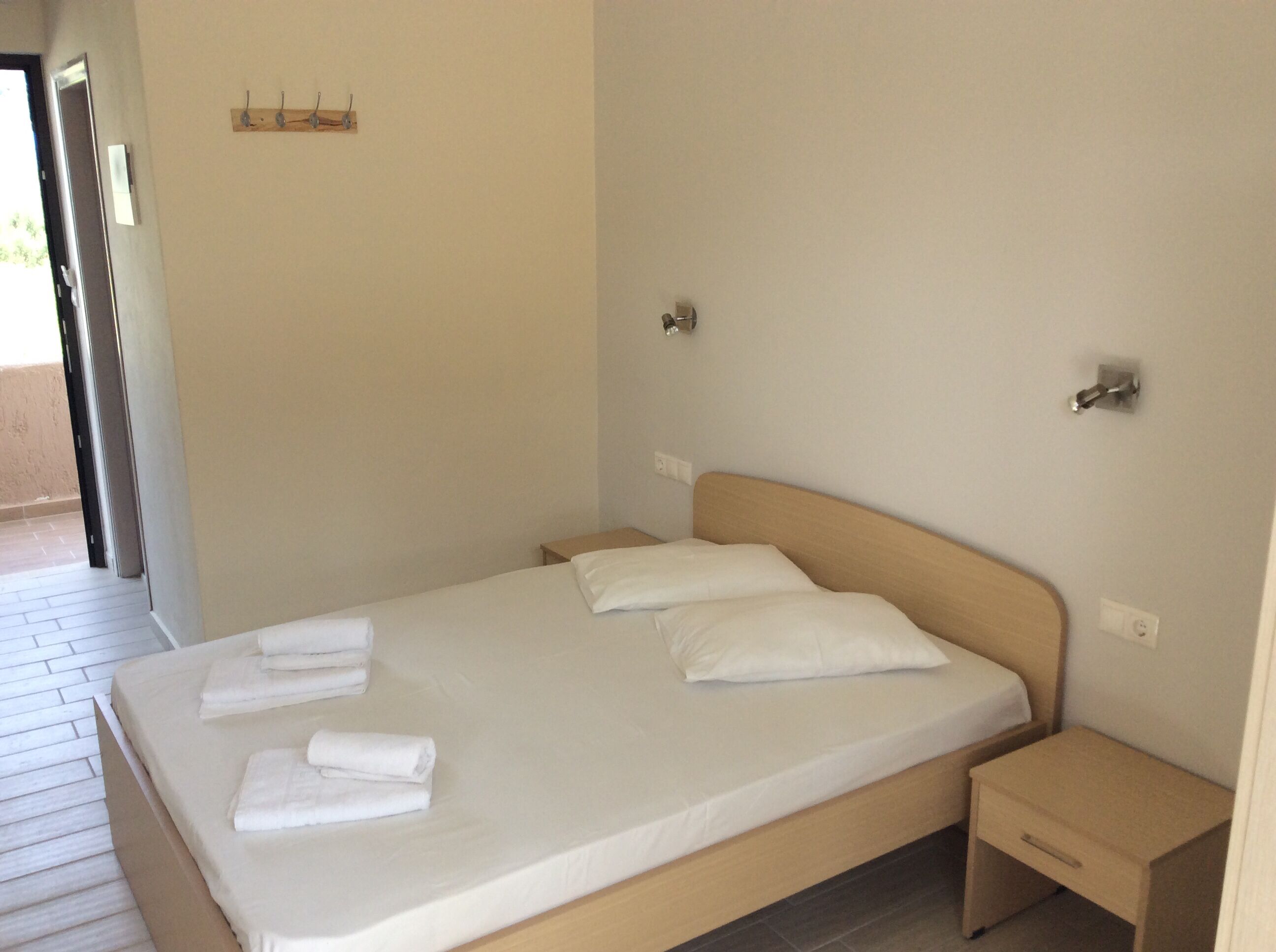 A neatly made bed with white linens and towels, a wooden headboard, and a small bedside table with a drawer.