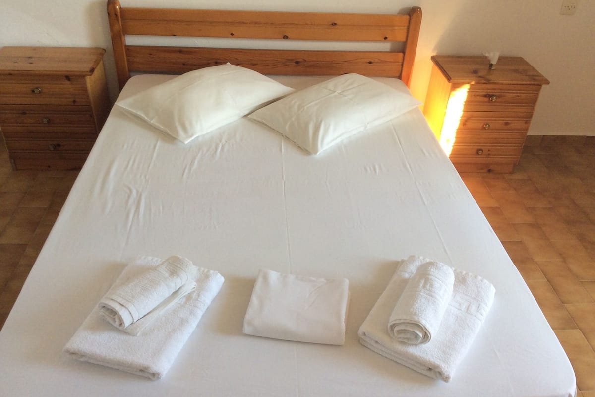 A neatly made bed with white linens and pillows, two wooden nightstands with drawers, and a wooden headboard.