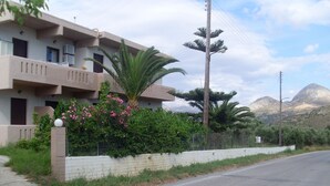A two-story building with balconies, a palm tree, and a mountain in the background. - Elena Rooms (Agios Vasileios)