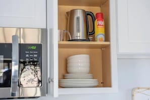 Una cocina con cafetera, hervidor y una pila de platos blancos.