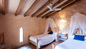 Un dormitorio con dos camas, vigas de madera, ventilador de techo, mesita de noche con lámpara y una ventana.
