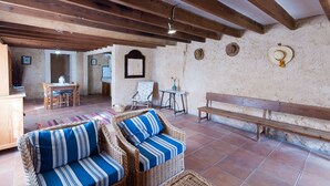 Un interior rústico con vigas de madera a la vista, mobiliario de mimbre y suelo de baldosas.