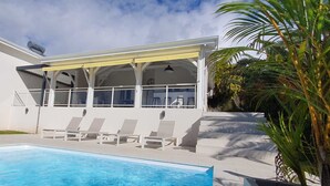 Et moderne hus med en pool, med en overdækket terrasse med liggestole og en trappe op til øvre etage.