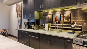 A modern kitchen with dark cabinetry, a central island with a sink, and a gas stove. - Outpost: Pearl at Jackson - Close to Town Square (Jackson)