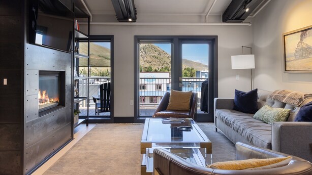 A modern living room with a fireplace, comfortable seating, and large windows offering a view of a hillside. - Outpost: Pearl at Jackson - Close to Town Square (Jackson)