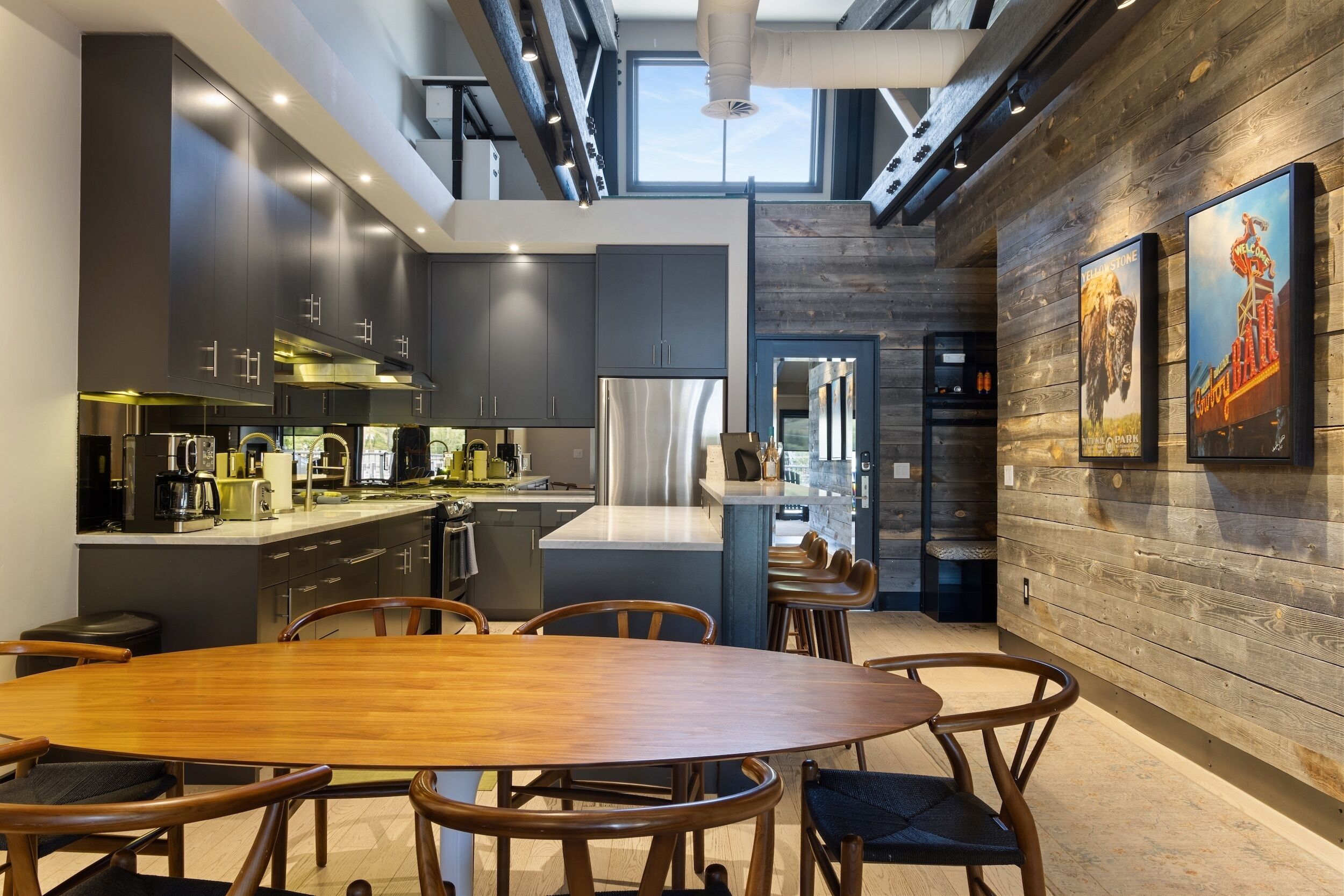 A modern kitchen with dark cabinets, stainless steel appliances, and a central island. There is a dining area with a wooden table and chairs.