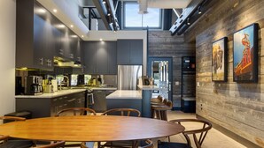 A modern kitchen with dark cabinets, stainless steel appliances, and a central island. There is a dining area with a wooden table and chairs. - Outpost: Pearl at Jackson - Close to Town Square (Jackson)