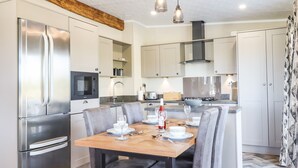 A modern kitchen with a built-in stove, a refrigerator, and a dining table set for four. - Cherry Lodge (Newton Abbot)