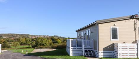 A single-story mobile home with a fenced porch and a small deck, set in a rural area with a clear sky.