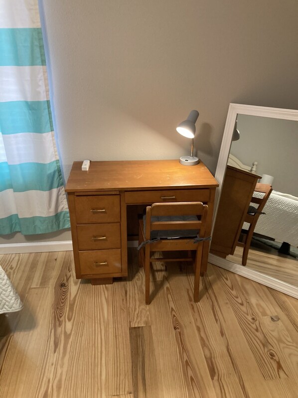 A wooden desk with a chair, a desk lamp, and a mirror.