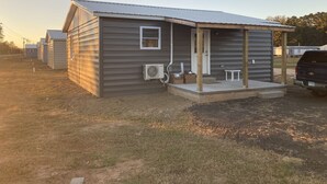 A single-story, gray wooden house with a covered porch, an air conditioning unit, and a truck parked nearby. - Fern’s Cottage New Construction! A cozy place to relax. (Atmore)