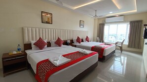 A hotel room with two beds, a ceiling fan, a window with curtains, and a nightstand with a water bottle. - Sri Aswin Grand (Namakkal)
