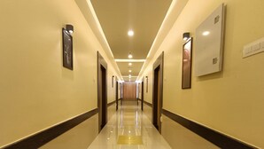 A hotel hallway with a reflective tiled floor, doors on both sides, and overhead lighting. - Sri Aswin Grand (Namakkal)